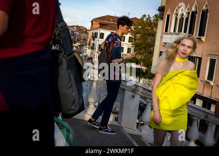 Le persone vengono ai ponti su Venezia per essere viste e ammirare il tramonto. Una donna con un vivace vestito giallo si fa strada attraverso un ponte sul Foto Stock