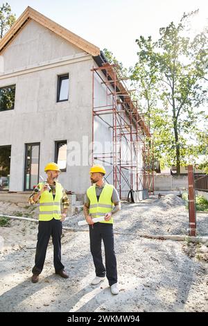 attraenti lavoratori edili devoti con livelli e progetti che si guardano l'un l'altro, costruttori Foto Stock