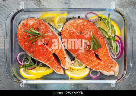 Bistecche di pesce rosso con vari ingredienti in un piatto da forno in vetro sul tavolo, vista dall'alto della trota fresca Foto Stock