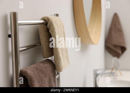 Portasciugamani riscaldato con asciugamani marroni in bagno, primo piano Foto Stock