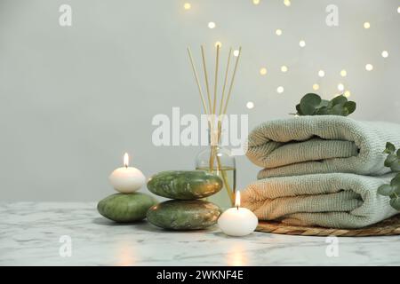 Composizione del centro benessere. Asciugamani, pietre, deodorante per ambienti a canne e candele accese su un tavolo in marmo bianco, spazio per testo Foto Stock