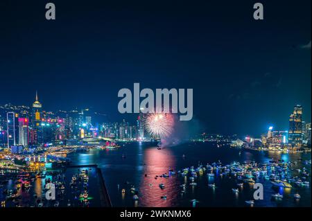 I fuochi d'artificio esplodono brillantemente contro il cielo notturno sopra lo skyline della città, riflettendo nelle acque calme sottostanti Foto Stock