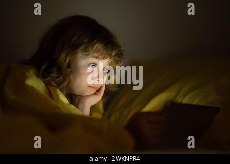 La storia del tempo a letto. Ragazzo che guarda un tablet prima di dormire. Il bambino legge l'e-book. Il bambino guarda lo schermo del tablet in alto. Ragazzo che gioca Foto Stock