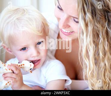 Sorridi, mamma e bambino con il giocattolo, il gioco e la famiglia si uniscono per lo sviluppo a casa. Mamma, bambino e bambino con giraffa per la partita Foto Stock