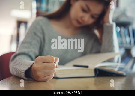 Studentessa stressata con pugno stringato che legge un libro a tavola, primo piano Foto Stock