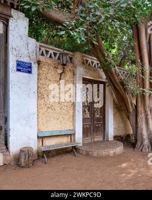 Panca blu in legno intemprato si trova invitante accanto ad una classica porta grunge decorata in legno. Una lampada in metallo d'epoca è appesa sopra la panca, per aggiungere un tocco nostalgico alla scena Foto Stock