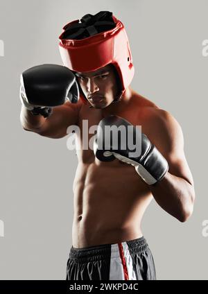 Uomo, ritratto e in studio con equipaggiamento da boxe per la sicurezza durante la lotta, duro e serio per la competizione. Uomo, abbigliamento protettivo e pronto per Foto Stock
