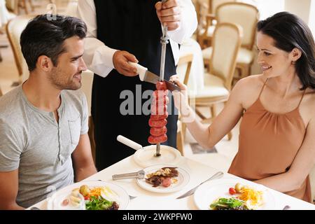 Ristorante di coppia e cameriere che serve cibo o kebab di salsiccia su spiedino per cene raffinate, anniversari o nutrizione. Uomo, donna e rapporto Foto Stock