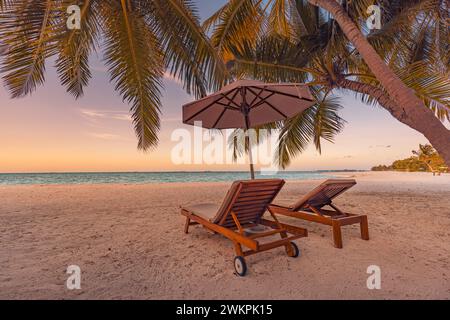 Splendida costa tropicale al tramonto, due lettini e ombrellone sotto le palme. Primo piano di sabbia bianca, orizzonte con vista sul mare, cielo colorato al crepuscolo calmo Foto Stock