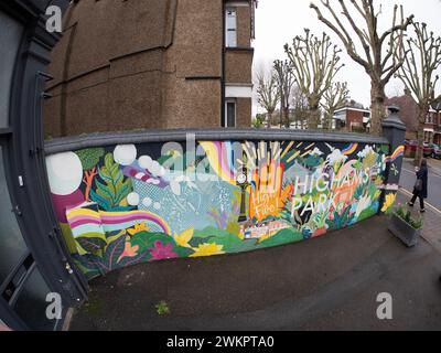 Un vivace murale di Street art dipinto su una parete esterna bianca sulla Avenue di Highams Park, Londra, Regno Unito, E4. Le opere d'arte raffigurano i monumenti locali e le scene dell'area di Highams Park, che fungono da opera d'arte pubblica concentrata sulla comunità nel cuore del quartiere. Situato nel London Borough of Waltham Forest, il murale contribuisce all'estetica suburbana della sfilata dello shopping vicino alla stazione ferroviaria di Highams Park Foto Stock