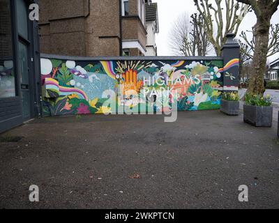 Un vivace murale di Street art dipinto su una parete esterna bianca sulla Avenue di Highams Park, Londra, Regno Unito, E4. Le opere d'arte raffigurano i monumenti locali e le scene dell'area di Highams Park, che fungono da opera d'arte pubblica concentrata sulla comunità nel cuore del quartiere. Situato nel London Borough of Waltham Forest, il murale contribuisce all'estetica suburbana della sfilata dello shopping vicino alla stazione ferroviaria di Highams Park Foto Stock