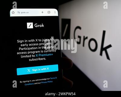 Persona che detiene un cellulare con pagina web del chatbot di intelligenza artificiale generativa Grok (X.ai) con logo. Messa a fuoco al centro del display del telefono. Foto Stock