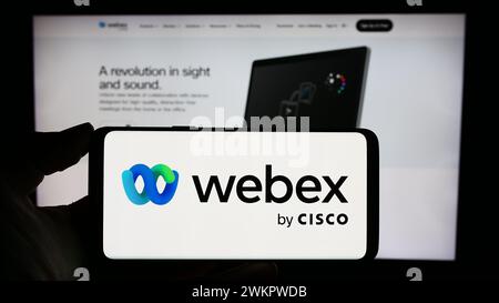 Persona che possiede un telefono cellulare con il logo della società americana di comunicazioni unificate Webex by Cisco davanti alla pagina Web. Mettere a fuoco il display del telefono. Foto Stock