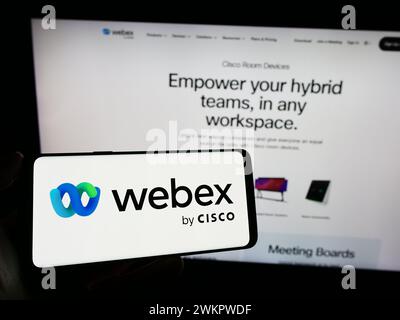 Persona che detiene un cellulare con il logo della società statunitense di comunicazioni unificate Webex by Cisco davanti alla pagina Web aziendale. Mettere a fuoco il display del telefono. Foto Stock