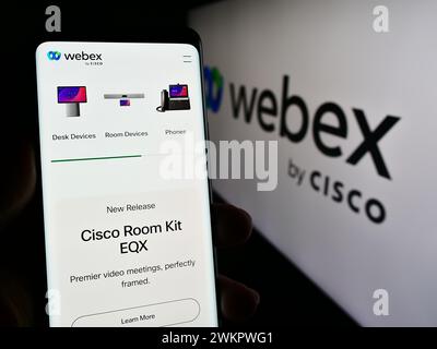 Persona che detiene un telefono cellulare con la pagina Web della società statunitense di comunicazioni unificate Webex by Cisco davanti al logo. Messa a fuoco al centro del display del telefono. Foto Stock