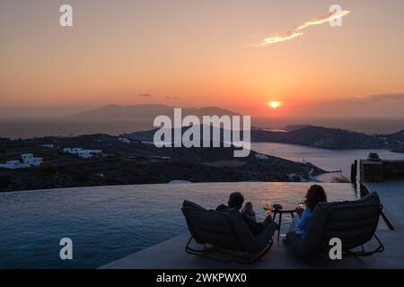 IOS, Grecia - 17 settembre 2023: Veduta di una coppia seduta davanti ad una piscina presso un lounge bar che si gode lo spettacolare tramonto a iOS Grecia Foto Stock