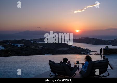 IOS, Grecia - 17 settembre 2023: Veduta di una coppia seduta davanti ad una piscina presso un lounge bar che si gode lo spettacolare tramonto a iOS Grecia Foto Stock