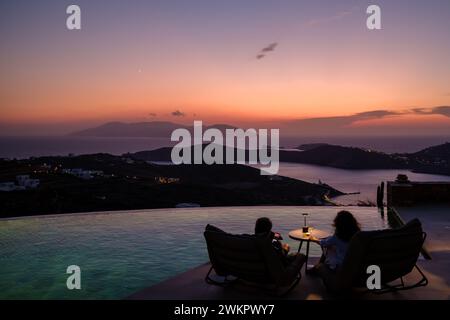 IOS, Grecia - 17 settembre 2023: Veduta di una coppia seduta davanti ad una piscina presso un lounge bar che si gode lo spettacolare tramonto a iOS Grecia Foto Stock