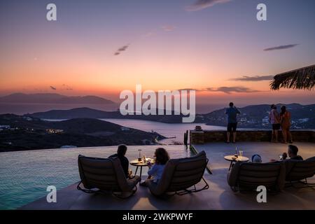 IOS, Grecia - 17 settembre 2023: Veduta di una coppia seduta davanti ad una piscina presso un lounge bar che si gode lo spettacolare tramonto a iOS Grecia Foto Stock