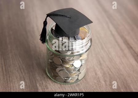 Vaso in vetro riempito di monete e un cappuccio graduato sopra. Copia spazio per il testo. Concetto di risparmio nel settore dell'istruzione. Foto Stock