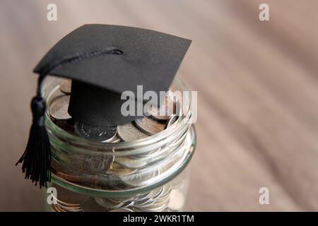 Vaso in vetro riempito di monete e un cappuccio graduato sopra. Copia spazio per il testo. Concetto di risparmio nel settore dell'istruzione. Foto Stock