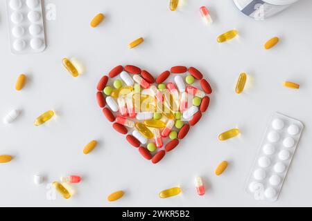 Gruppo di pillole in diversi colori disposte a forma di cuore su sfondo bianco. Concetto medico di assistenza sanitaria umana. Foto Stock