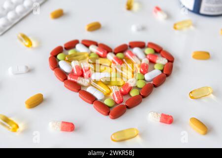 Gruppo di pillole in diversi colori disposte a forma di cuore su sfondo bianco. Concetto medico di assistenza sanitaria umana. Foto Stock