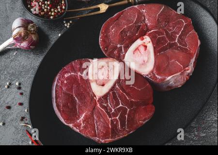 Ossobuco grezzo. Codoli di vitello ossobuco con pepe, limone e aglio per la gremolata, ingredienti tipici della cucina lombarda italiana, vista dall'alto sul dorso scuro Foto Stock