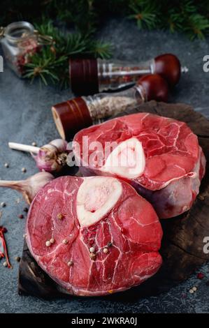 Ossobuco grezzo. Codoli di vitello ossobuco con pepe, limone e aglio per la gremolata, ingredienti tipici della cucina lombarda italiana, vista dall'alto sul dorso scuro Foto Stock