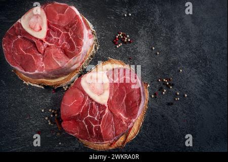 Ossobuco grezzo. Codoli di vitello ossobuco con pepe, limone e aglio per la gremolata, ingredienti tipici della cucina lombarda italiana, vista dall'alto sul dorso scuro Foto Stock