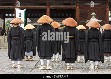 Nagano, Giappone. Monaci buddisti Zen giapponesi della scuola Soto con cappelli Kasa che guardano la porta Sanmon di Zenko-ji, un tempio buddista Foto Stock