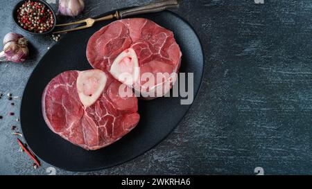 Ossobuco grezzo. Codoli di vitello ossobuco con pepe, limone e aglio per la gremolata, ingredienti tipici della cucina lombarda italiana, vista dall'alto sul dorso scuro Foto Stock