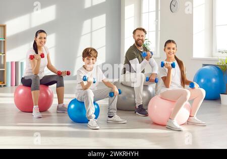 Ritratto di una famiglia felice che fa esercizi sportivi in palestra seduti su palle e tenendo in mano i manubri. Foto Stock