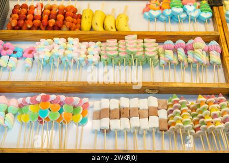 Una deliziosa selezione di coloratissimi spiedini di caramelle, tra cui marshmallow e caramelle in gelatina, esposti in un bancone del mercato in vendita Foto Stock