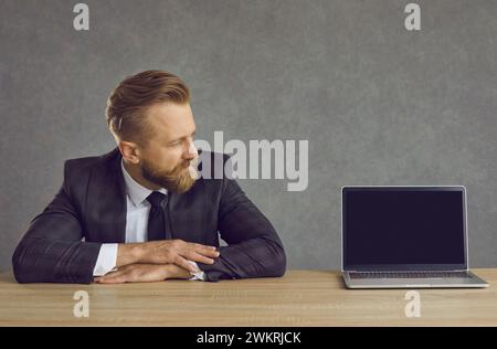 Uomo d'affari caucasico seduto al tavolo e guardando lo schermo nero del notebook Foto Stock