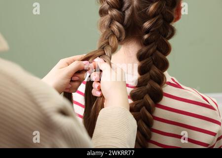 Stilista professionista che intreccia i capelli di donna su sfondo color oliva, primo piano Foto Stock