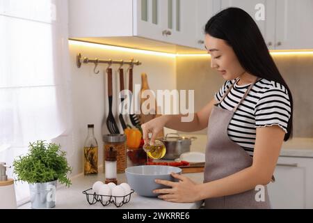 Processo di cottura. Bella donna che versa l'olio dalla bottiglia alla ciotola in cucina Foto Stock