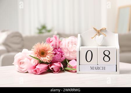 Giornata internazionale della donna - 8 marzo. Calendario a blocchi e bouquet di splendidi fiori su un tavolo di legno bianco Foto Stock