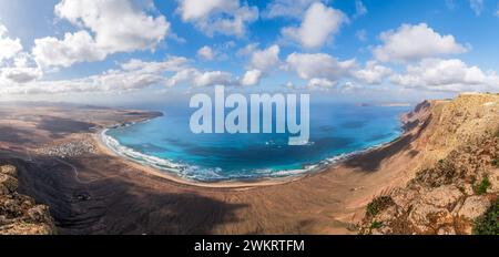 Ampie vedute di Playa Famara, Lanzarote, con le sue sabbie dorate abbracciate da acque azzurre e scogliere spettacolari, un paradiso per i surfisti. Foto Stock