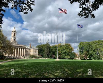 State College, Pennsylvania, USA – 7 ottobre 2023: Vecchio edificio principale del campus della Penn State University, Pennsylvania, in una giornata nuvolosa, con bandiere ondulate Foto Stock