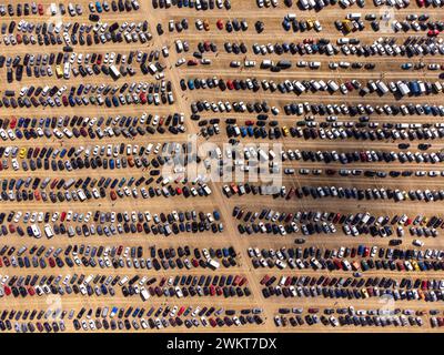 Colpo di droni dall'alto che cattura il caos organizzato di veicoli parcheggiati in un parcheggio all'aperto sotto la luce del sole. Foto Stock