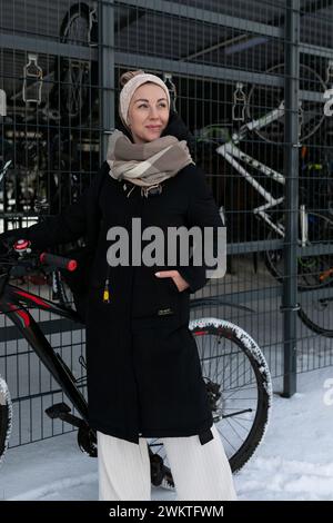 Una donna sorridente con dreadlock biondi ha noleggiato una bicicletta in inverno Foto Stock