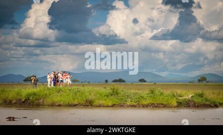 Un gruppo di turisti che scattano foto su smartphone si affollano per ammirare un coccodrillo del Nilo nel Parco Nazionale di Mikumi in Tanzania. Foto Stock