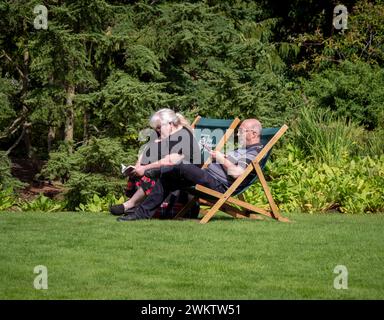 Coppia matura seduta su sedie a sdraio godendosi il sole in un giardino RHS. REGNO UNITO Foto Stock