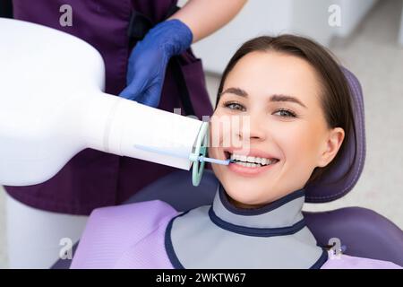 Una paziente sorride mentre riceve una radiografia dei denti presso la clinica odontoiatrica Foto Stock