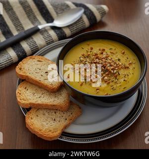 Una crema di zucca con aglio servita con tre pezzi di pane tostato in una ciotola nera Foto Stock