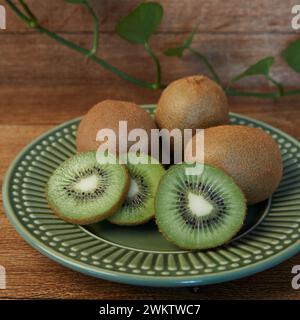 Alcuni kiwi interi e tagliati all'interno di un piatto verde su uno sfondo di legno Foto Stock