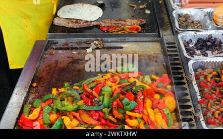 Peperoni gialli rossi e verdi sfrigolanti sulla piastra calda di uno stand di Street food che cucina con le spezie Foto Stock