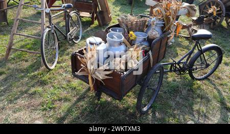 lattine di latte in alluminio intemperie traboccanti di prodotti freschi agricoli in un carrello di legno con bicicletta Foto Stock