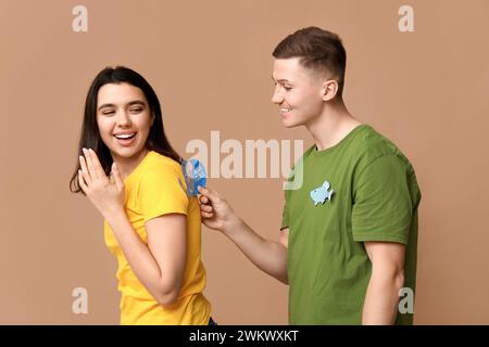 Giovane che attacca carta sulla schiena del suo amico su sfondo marrone. Festa del giorno dello scemo d'aprile Foto Stock